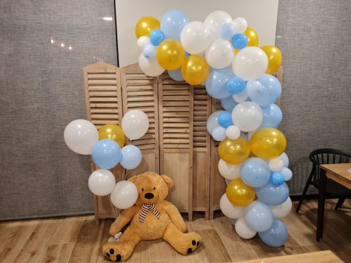 Arco de globos en azul, blanco y amarillo con un oso de peluche sentado.