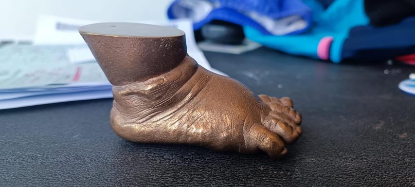Escultura de un pie en tono marrón, con detalles en los dedos y el tobillo.
